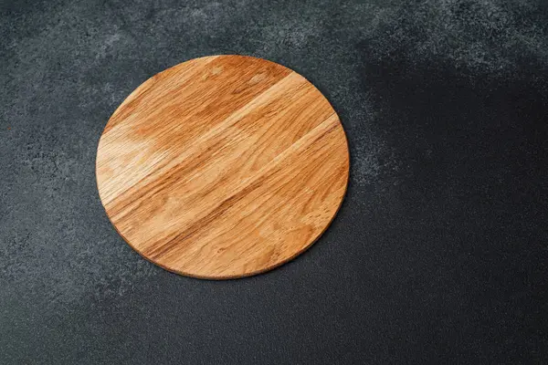 Yuvarlak ahşap bir tahta, yemek servisi için ideal, karanlık bir taş yüzeyde bulunur..
