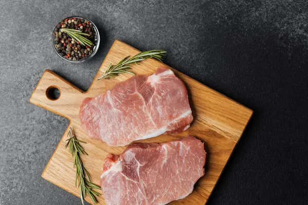 İki çiğ domuz bifteği ahşap bir kesim tahtasına konur. Bitki ve baharatlarla birlikte..