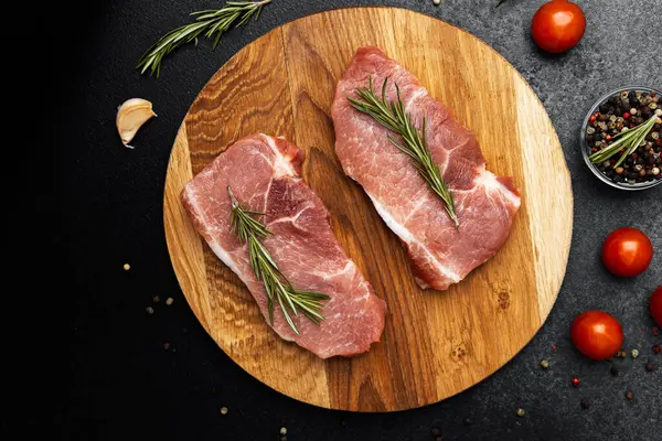 Biberiyeyle süslenmiş ve domates ve baharatlarla çevrili taze domuz dilimleri..