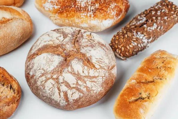 Beyaz bir yüzeye düzgün bir şekilde yerleştirilmiş çeşitli taze ekmek türleri.