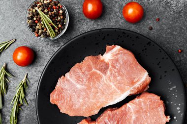 Siyah bir tabakta domuz pirzolası ve yanında da vişneli domates ve baharat..