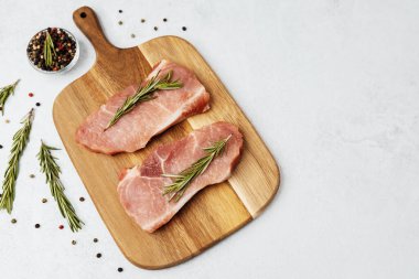 İki çiğ domuz pirzolası, ahşap kesme tahtasının üzerinde taze biberiyeyle süslenmiş.