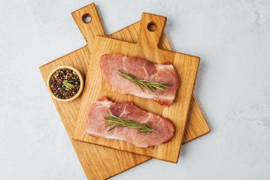 İki domuz pirzolası, ahşap kesme tahtalarında biberiye ve baharatla süslenmiş..