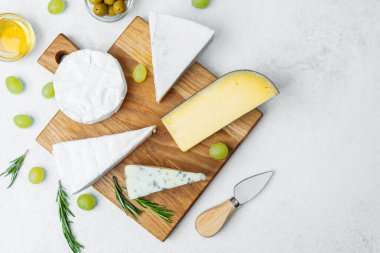 Taze peynirler ahşap kesim tahtasına yerleştirilmiş üzümler ve zeytinlerle.