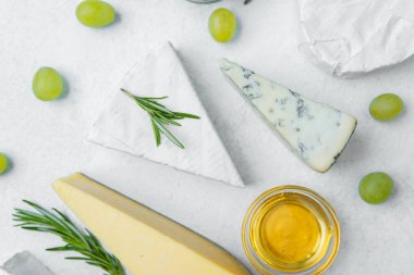 Beyaz bir yüzeye yerleştirilmiş üzüm ve bal ile sıralanmış çeşitli peynirler.