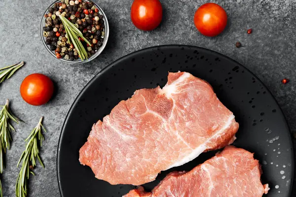 Siyah bir tabakta domuz pirzolası ve yanında da vişneli domates ve baharat..