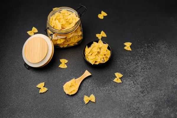 Daha fazla pişmemiş makarna dolu bir kavanozun yanına saçılmış makarna..