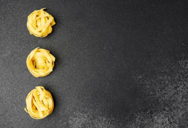 Üç pişmemiş fettucine makarnası desenli koyu bir yüzeye yerleştirilmiş..