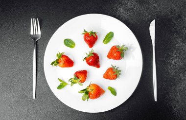 Parlak kırmızı çilekler, yaratıcı bir şekilde naneyle süslenmiş bir tabağa konur..