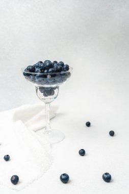 Yaban mersinleri şeffaf bir kaseyi hafif bir yüzeyde dağınık böğürtlenlerle doldurur..