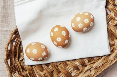 Hasır sepetinde papatya çiçekleri olan el yapımı Paskalya yumurtaları. Şenlikli kutlama için kırsal bahar kompozisyonu