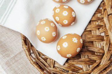 Hasır sepetinde papatya çiçekleri olan el yapımı Paskalya yumurtaları. Şenlikli kutlama için kırsal bahar kompozisyonu.