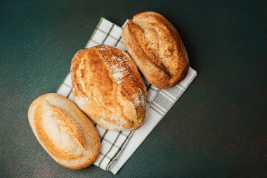 Konforlu bir mutfaktaki kareli kumaş üzerinde sergilenen üç çeşit zanaatkar ekmek..