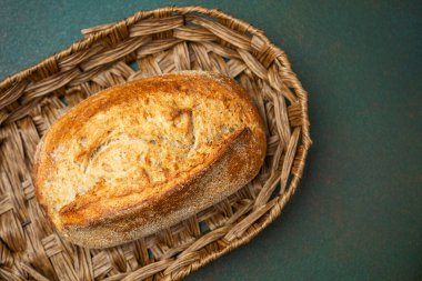 Bir somun zanaatkar ekmeği dokuma sepetinde duruyor, kabuklu yüzeyini vurguluyor..