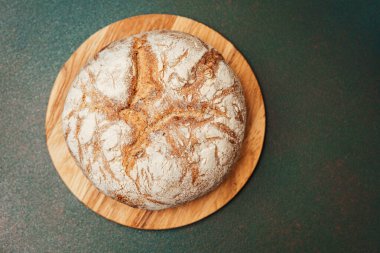 Köy ekmeği ahşap bir kesme tahtasının üzerinde duruyor, kabuğunu gösteriyor..