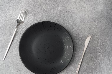 Basit bir siyah plaka gri yüzeyde çatal ve bıçakla çevrilidir..