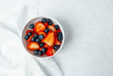 Hafif arkaplanda canlı çilekler ve yabanmersinleriyle dolu bir kase..