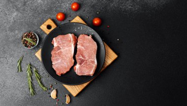 Sulu domuz pirzolası taze otlar ve domateslerle çevrili siyah bir tabakta dinleniyor..