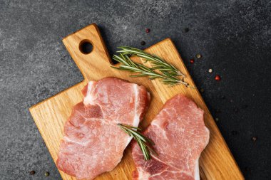 Domuz pirzolası, biberiye ve baharatlarla dolu bir kesme tahtasının üzerinde duruyor..