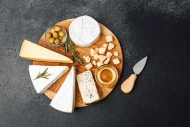 Tahta bir tahtanın üzerinde güzel bir şekilde düzenlenmiş peynir, zeytin ve bal seçimi..