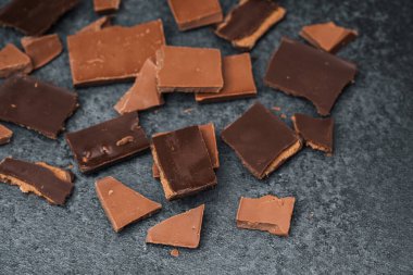 Çeşit çeşit çikolata parçaları koyu bir yüzeye dağılmış, eşsiz dokular sergiliyor..