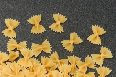 Mutfak kullanımı için siyah bir yüzeye yerleştirilmiş çeşitli kuru farfalle makarna parçaları..