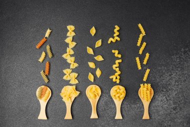 Tahta kaşıklarda gösterilen farklı makarna şekilleri çekici bir mutfak düzeni oluşturur..