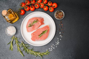 Beyaz seramik tabakta çiğ biftek, domates, tuz ve biber.