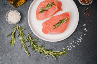 Beyaz seramik tabakta çiğ biftek, domates, tuz ve biber.