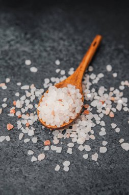 Ahşap kaşık pembe himalaya tuzu ve dokulu siyah yüzey.