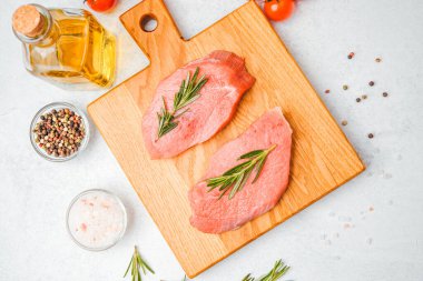 Domates, yağ, tuz ve biberiye ile çevrili ahşap kesim tahtasıyla çiğ dana bifteği.