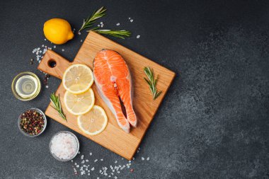 Limon dilimleri ve bitkilerle birlikte kesme tahtasına yerleştirilmiş taze somon filetosu..