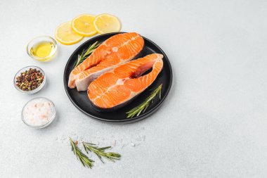 Somon filetosu, limon dilimleri ve baharatlarla birlikte siyah bir tabakta dinleniyor..