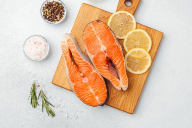 Somon filetoları, limon dilimleri ve otlarla birlikte bir kesim tahtasının üzerinde sergilenir..