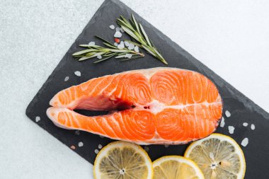 Limon dilimleri ve koyu bir yüzeyde taze otlarla sergilenen somon bifteği..