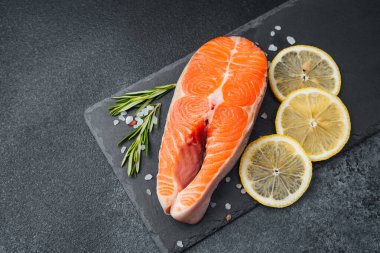 Limon dilimleri ve biberiyenin yanında taze kesilmiş somon filetosu..