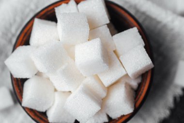 Beyaz şeker küpleri kahverengi bir kasede desenli kumaş bir yüzeye istiflenmiş..