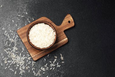 Tahta kesme tahtasının etrafında gevşek tanecikler olan beyaz pirinçle dolu bir kase..