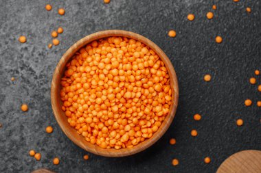 Parlak turuncu mercimekler, siyah bir tezgahın üzerindeki yuvarlak ahşap bir kaseye konur..