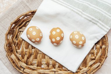 Hasır sepetinde papatya çiçekleri olan el yapımı Paskalya yumurtaları. Şenlikli kutlama için kırsal bahar kompozisyonu
