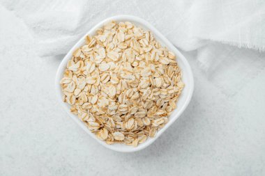 Pişmemiş yulaflarla dolu bir kase pürüzsüz, hafif bir yüzeye yerleştirilmiş..