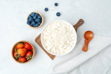 Taze çilek ve böğürtlenlerle çevrili bir tabak süzme peynir..