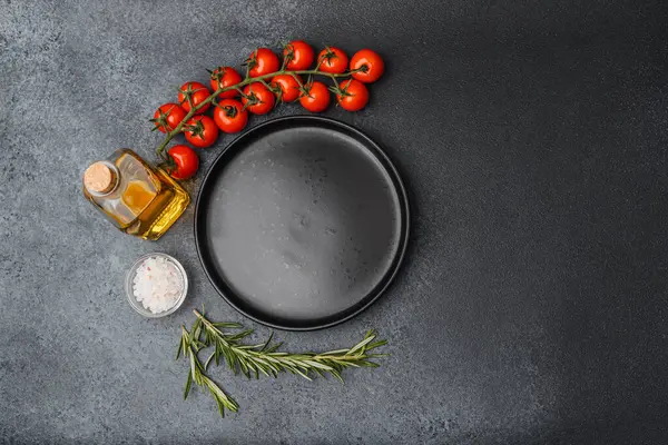 Boş siyah tabak, kirazlı domates zeytinyağı biberiye tuzu ve siyah arka planda biber.