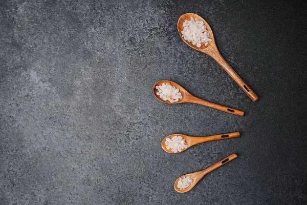 Siyah zemin üzerinde pembe himalaya tuzu olan tahta kaşıklar.