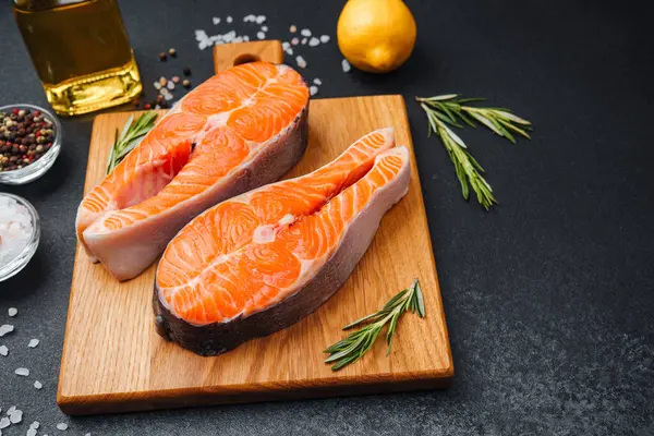 Tahta kesme tahtasına yerleştirilmiş iki somon filetosu ve yanında da otlar ve baharatlar..