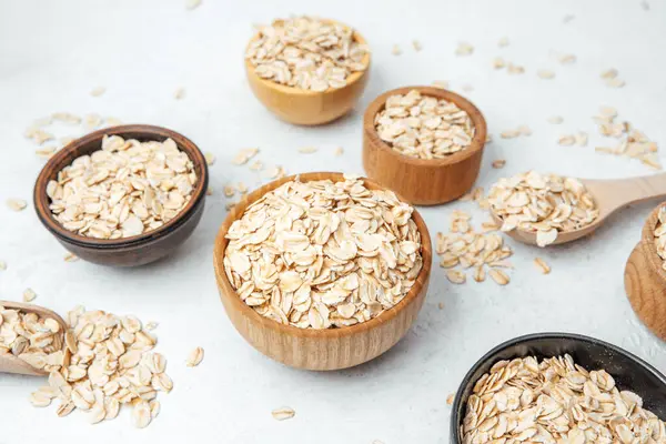 Yulaf dolu çeşitli kaseler yemek pişirmek için beyaz bir yüzey üzerinde sergilenir.