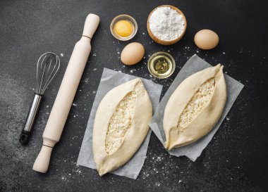 Malzemelerin üst görüntüsü ve iki pişmemiş khachapuri un kaplı siyah masa üzerinde