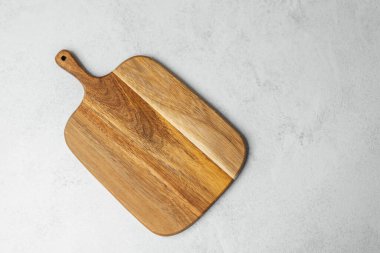 Ahşap kesme tahtası açık gri bir zeminde yemek pişirmek için gerekli malzemeleri bekliyor..