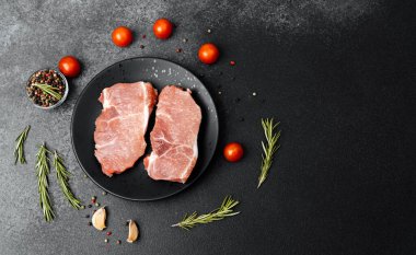 Siyah bir tabakta domuz pirzolası ve kiraz domatesleri pişmeye hazır..