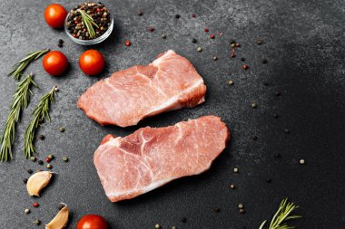 İki domuz pirzolası, domates, sarımsak ve baharatlarla karanlık bir yüzeye yerleştirilir..